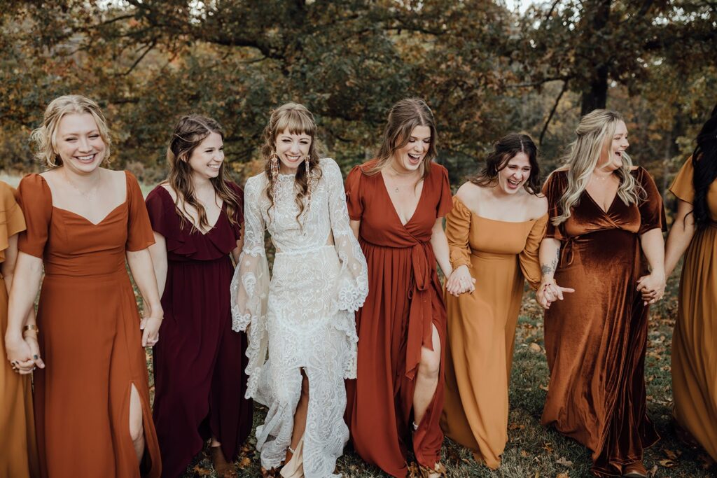Bride in white dress with her bridesmaids in copper, terracotta, gold, and bronze dresses.