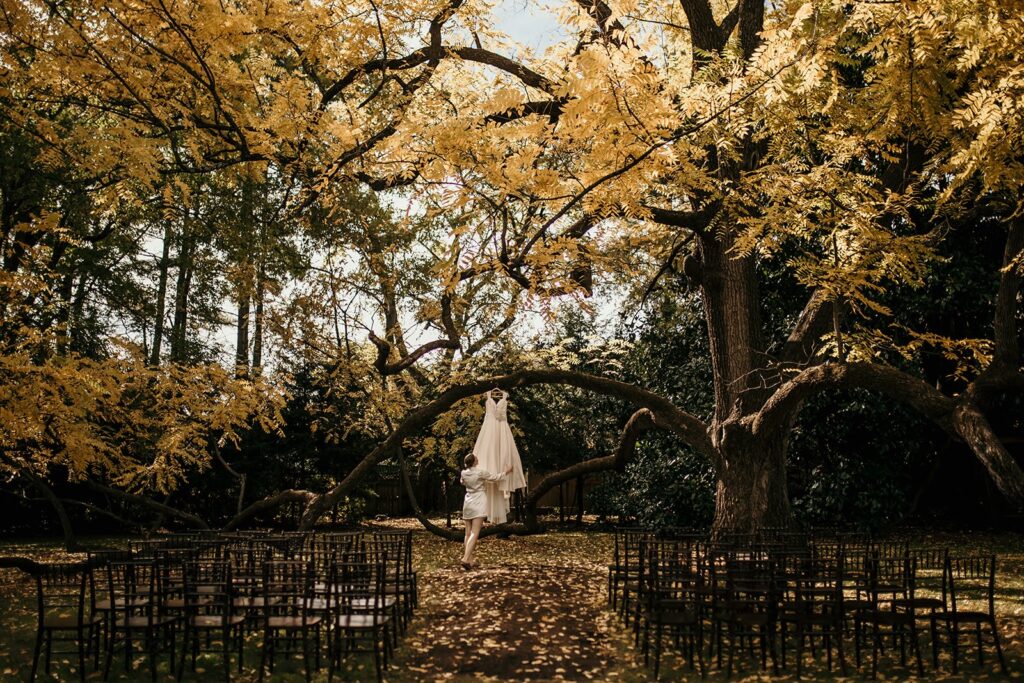A bride in a robe looking at her dress as it hanging in a large magnolia tree at her ceremony site.